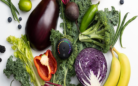 Nu Skin PRYSM iO handheld antioxidant scanner resting on a variety of fresh, colorful vegetables.
